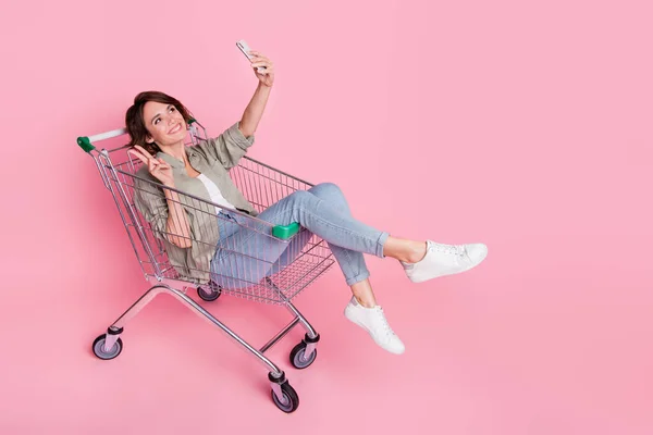 Повний профіль тіла фотографія молодої леді їздити на ринку кошик зробити селфі мобільне шоу v-символ ізольовані на рожевому кольоровому фоні — стокове фото