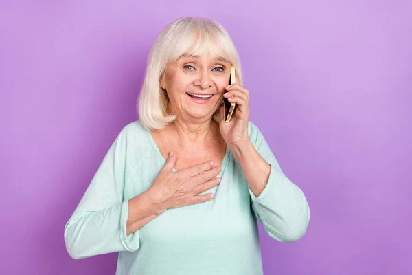 Foto de engraçado grata velho vovó segurar telefone ouvir boas notícias desgaste camisa azul isolado cor violeta fundo — Fotografia de Stock