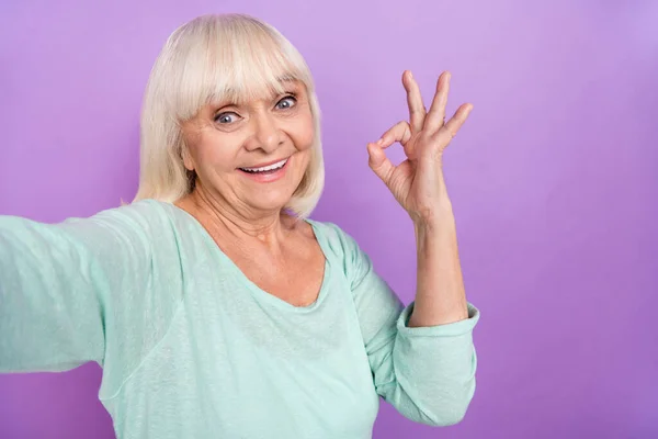 Фотографія надійної пенсіонерки, яка тримає камерне шоу символ джакузі, береться за сорочку для сліз, ізольований фіолетовий кольоровий фон — стокове фото