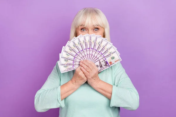 Foto di divertente pazzo pensionato bella vecchia signora tenere contante copertura del ventilatore faccia indossare camicia blu isolato colore viola sfondo — Foto Stock