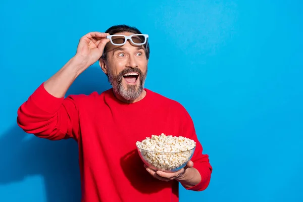 Retrato de homem alegre atraente comendo milho assistindo vídeo se divertindo isolado sobre fundo de cor azul brilhante — Fotografia de Stock