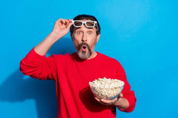 Retrato de atraente alegre engraçado surpreendido homem comendo milho assistindo vídeo isolado sobre fundo de cor azul brilhante — Fotografia de Stock
