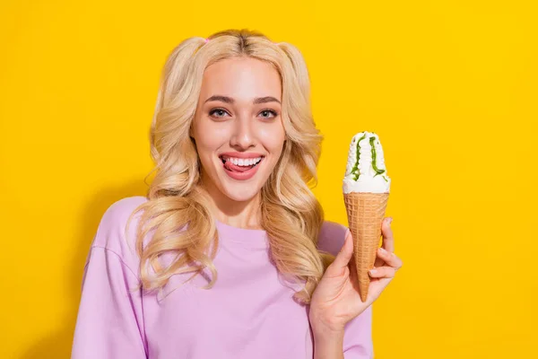Retrato de alegre bonito menina língua lamber dentes segurar sorvete olhar câmera isolada no fundo de cor amarela — Fotografia de Stock