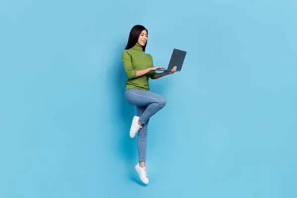 Foto corpo pieno di funky millennial bruna signora salto con il computer portatile usura maglione jeans scarpe da ginnastica isolato su sfondo blu — Foto Stock