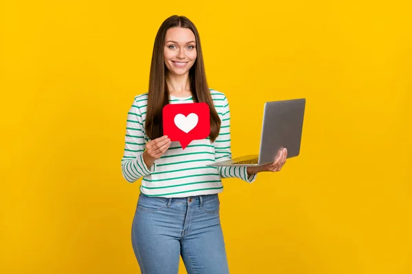 Foto de encantadora senhora brilhante vestida camisa listrada segurando dispositivo moderno cartão cardíaco isolado cor amarela fundo — Fotografia de Stock