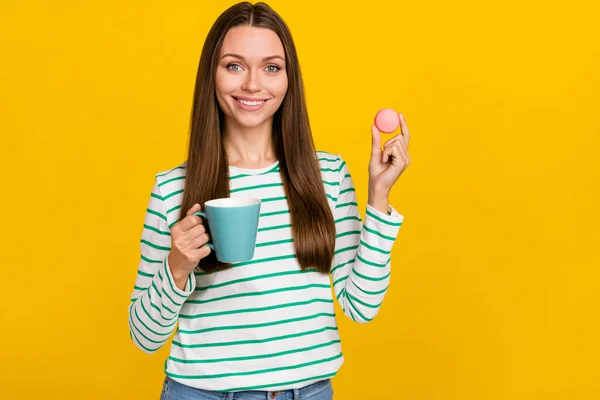 Foto de bonito engraçado jovem mulher usar camisa listrada beber chá comer bolo isolado cor amarela fundo — Fotografia de Stock