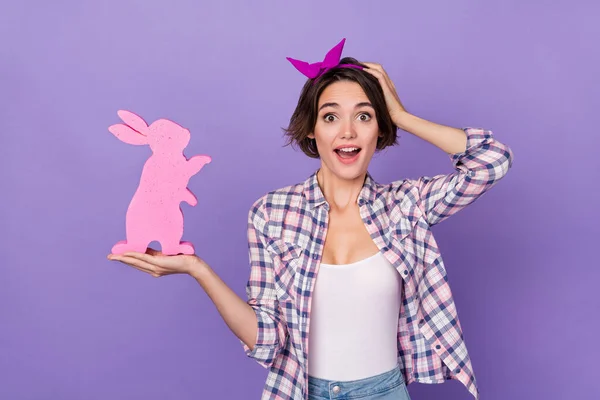 Foto de mujer divertida impresionada usar camisa a cuadros sosteniendo conejo rosa brazo cabeza aislado color violeta fondo —  Fotos de Stock