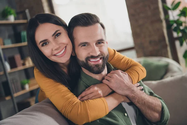 Retrato de pareja alegre atractiva abrazo pasar vacaciones sentado en el sofá divirtiéndose en casa casa plana en el interior —  Fotos de Stock