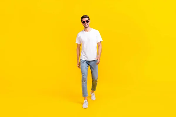 Full size photo of nice young brunet guy go wear spectacled t-shirt jeans sneakers isolated on yellow color background — Zdjęcie stockowe