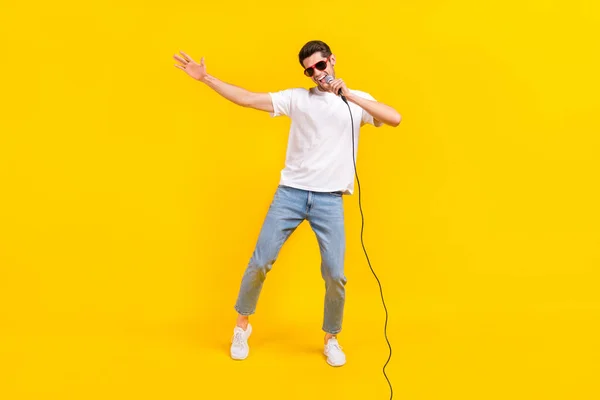 Full size photo of nice millennial brunet guy dance sing wear eyewear t-shirt jeans shoes isolated on yellow background — Stockfoto