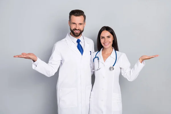 Foto van vrij gelukkig twee artsen dragen witte jassen vergelijken armen lege ruimte knuffelen geïsoleerde grijze kleur achtergrond — Stockfoto