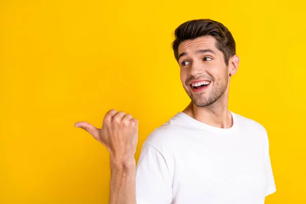 Photo of funky young brunet guy indicate empty space wear white t-shirt isolated on yellow color background — Stockfoto