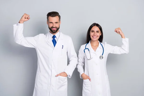 Retrato de dos médicos alegres exitosos atractivos demostrando músculos de poder aislados sobre fondo pastel de color gris — Foto de Stock