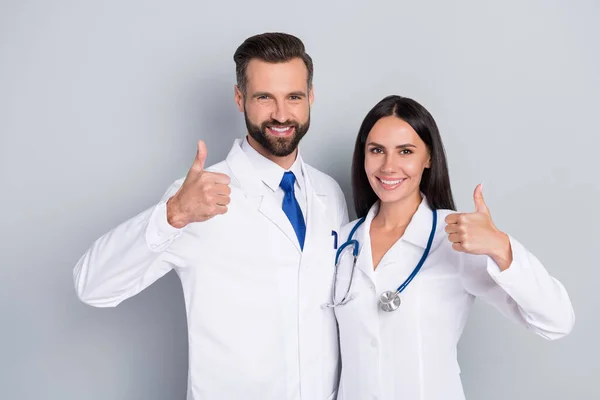 Foto von smart glücklich zwei Doktoren gekleidet weißen Mäntel umarmen zeigt Daumen nach oben isolierte graue Farbe Hintergrund — Stockfoto