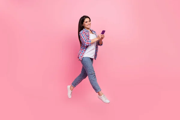 Pełny rozmiar zdjęcie Dojrzałe brunetka lady run trzymać telefon nosić koszulę dżinsy obuwie izolowane na różowym tle — Zdjęcie stockowe