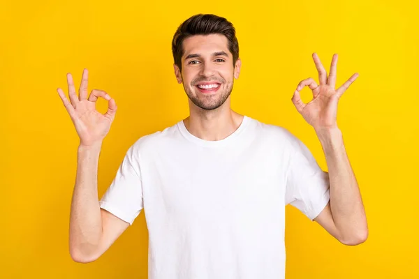 Фото впевненого привабливого чоловіка, який показує два знаки джека, носять білу футболку ізольований жовтий кольоровий фон — стокове фото