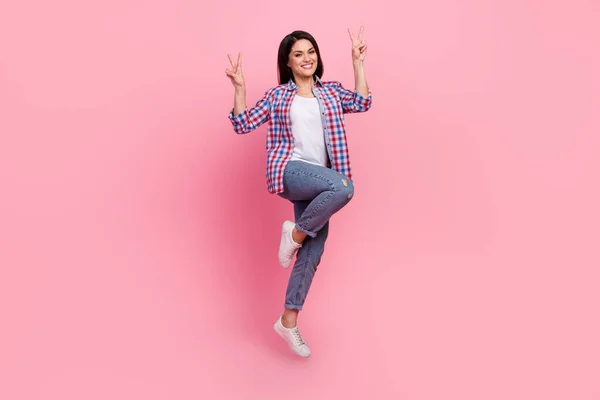 Full body foto di giovane bruna signora spettacolo v-segno salto usura camicia jeans calzature isolato su sfondo rosa — Foto Stock
