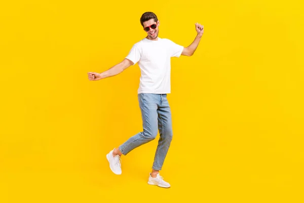 Foto de tamaño completo de divertido millennial morena chico danza desgaste gafas camiseta jeans zapatillas aisladas sobre fondo amarillo — Foto de Stock