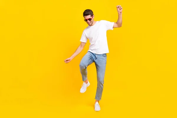 Foto de corpo inteiro de legal jovem morena cara dança desgaste óculos t-shirt jeans sapatos isolados no fundo amarelo — Fotografia de Stock