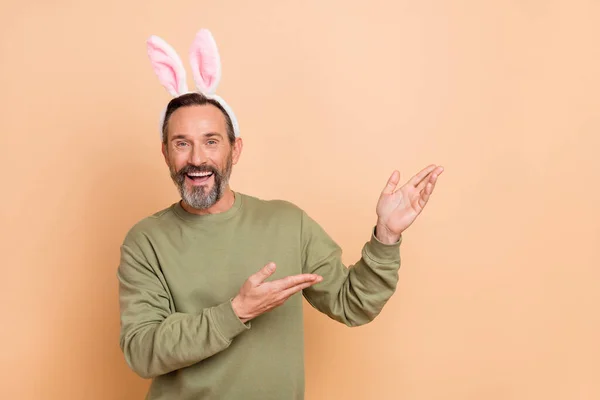 Porträt eines attraktiven, verspielten, fröhlichen Mannes mit Ohren, der Kopierraum isoliert über beige pastellfarbenem Hintergrund demonstriert — Stockfoto