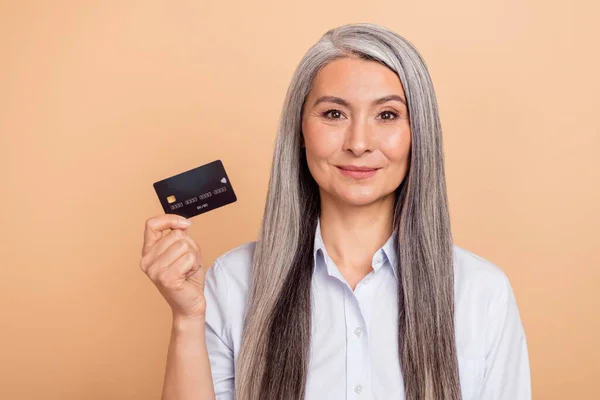 Foto di donna anziana in possesso di carta di credito salario benefici di risparmio isolato su sfondo di colore beige — Foto Stock