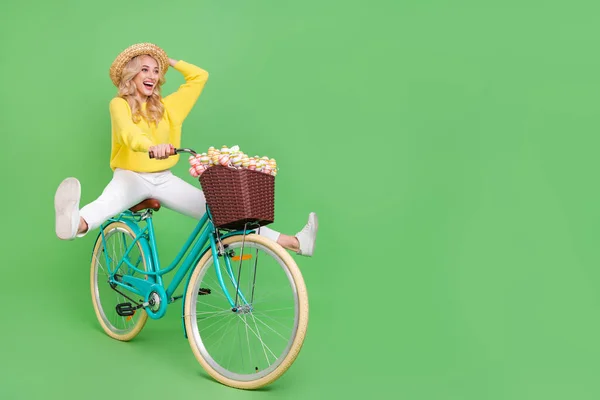 Photo of dreamy excited lady dressed yellow pullover headwear driving cycle empty space isolated green color background