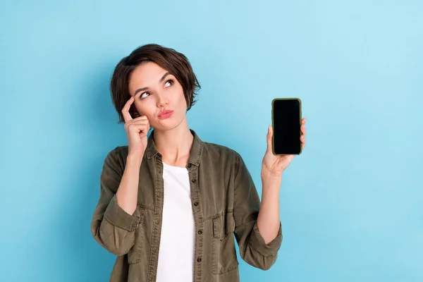 思考の写真若い短い髪型の女性は電話を保持見てプロモーションは、青の色の背景に隔離されたカーキシャツを着用 — ストック写真