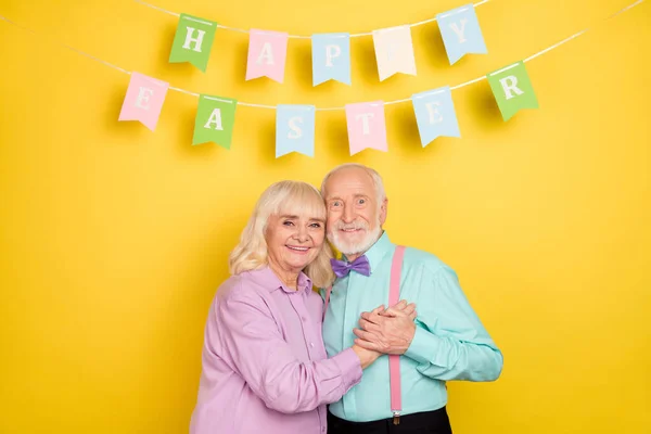 Πορτρέτο των δύο ελκυστικών χαρούμενα γκρίζα μαλλιά συζύγους αγκαλιάζει Πάσχα ημέρα απομονωμένη πάνω από φωτεινό κίτρινο χρώμα φόντο — Φωτογραφία Αρχείου