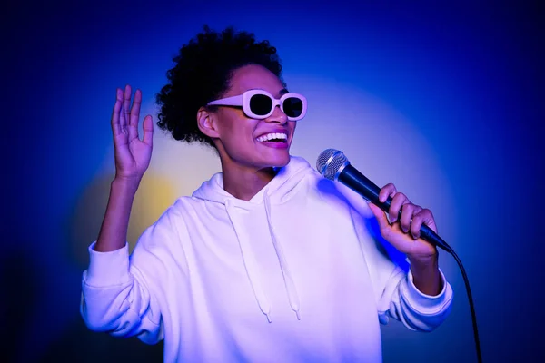 Fénykép bájos funky hölgy öltözött kapucnis sötét szemüveg ének dal elszigetelt kék szín háttér — Stock Fotó