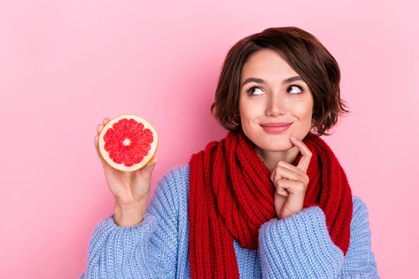 Fotografie smýšlející hezká dáma prst na bradě vypadat prázdné místo držet půl grapefruit izolované na růžové barevné pozadí — Stock fotografie