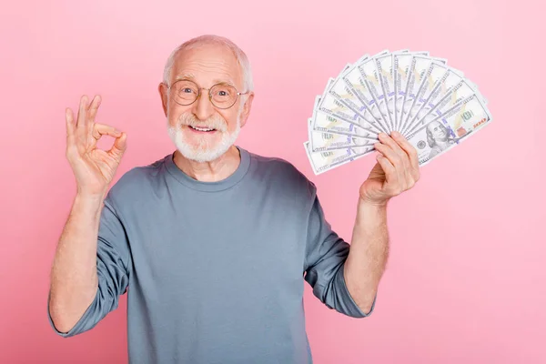 Foto di allegro carino pensionato uomo grigio maglione occhiali crescente contanti ventilatore okey segno isolato colore rosa sfondo — Foto Stock