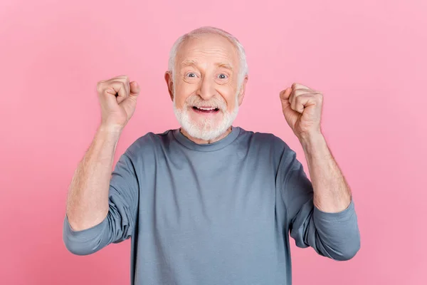 Fotografie šťastného vzrušený chlap důchodce oblečený šedý svetr usmívající se rostoucí pěsti izolované růžové barvy pozadí — Stock fotografie