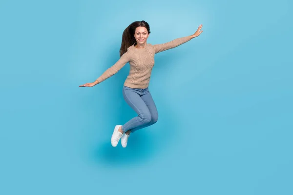 Foto av glada trevlig dam hoppa höja händerna bära beige tröja jeans sneakers isolerad blå färg bakgrund — Stockfoto
