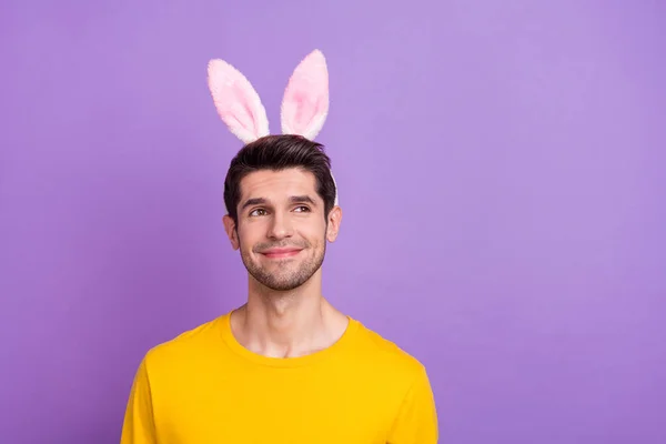 Foto van schattig goed humeur jonge man met grappige konijnenoren kijken lege ruimte dagdromen geïsoleerd op violette kleur achtergrond — Stockfoto