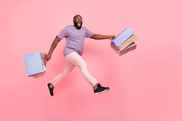 Fotografie zapůsobilo vzrušený chlap oblečený fialové tričko běží držení nakupujících prázdný prostor izolované růžové barvy pozadí — Stock fotografie