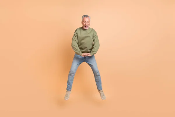 Foto de tamaño completo de lindo viejo gris peinado hombre salto desgaste jersey jeans zapatillas aisladas sobre fondo beige —  Fotos de Stock