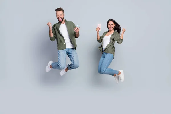 Volledige lengte foto van opgewonden man dame blogger springen vuisten tot web loterij overwinning gebruik gadget geïsoleerd op grijze kleur achtergrond — Stockfoto