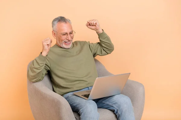 Zdjęcie hura stary siwy włosów człowiek siedzieć wygląd laptop nosić okulary pullover dżinsy izolowane na beżowym tle — Zdjęcie stockowe
