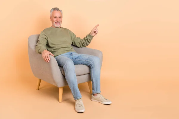 Pełna długość zdjęcie ładne stare siwe włosy człowiek siedzieć indeks promocyjne nosić pulowery dżinsy obuwie izolowane na beżowym tle — Zdjęcie stockowe