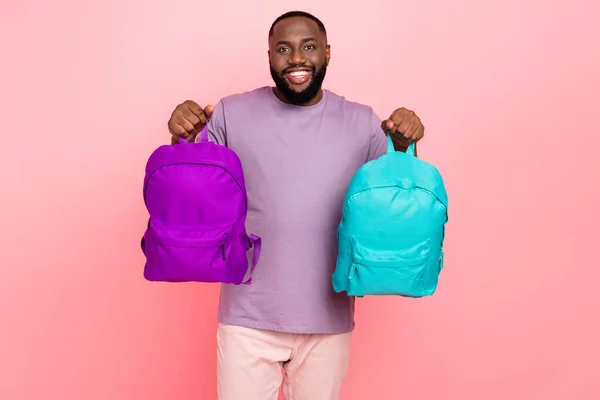 Foto van vrij grappige man dragen paars t-holding twee schooltassen glimlachen geïsoleerde roze kleur achtergrond — Stockfoto