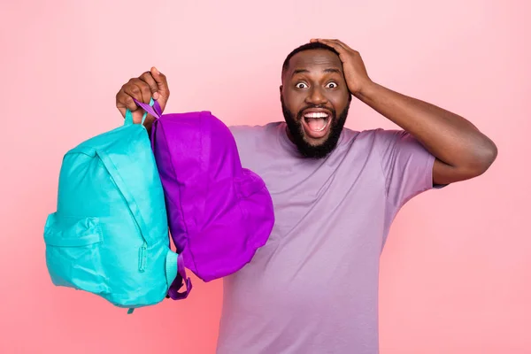 Foto van grappige onder de indruk man dragen paars t-shirt rijzen twee schooltassen arm hoofd geïsoleerde roze kleur achtergrond — Stockfoto