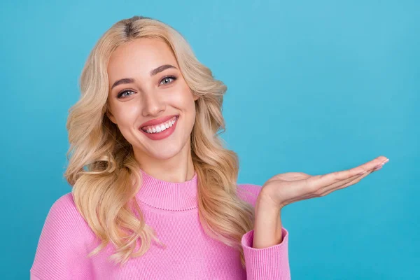 Foto von schönen Millennial blonde Dame halten leeren Raum tragen rosa Pullover isoliert auf blauem Hintergrund — Stockfoto