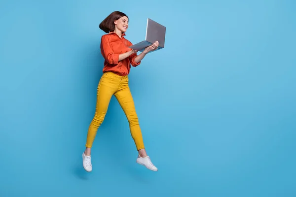 밝은 청색 배경 위에 분리 된 노트북을 사용하여 점프하는 매력적 인 쾌활 한 소녀의 전체 몸길이 사진 — 스톡 사진
