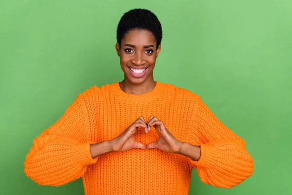 Zdjęcie słodkie millenium brunetka pani pokazać serce nosić pomarańczowy sweter izolowane na zielonym tle kolor — Zdjęcie stockowe