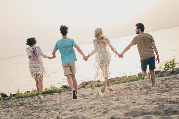 Foto de jovens positivos segurar braços corrida areia costa desgaste boho roupa natureza praia à beira-mar fora — Fotografia de Stock