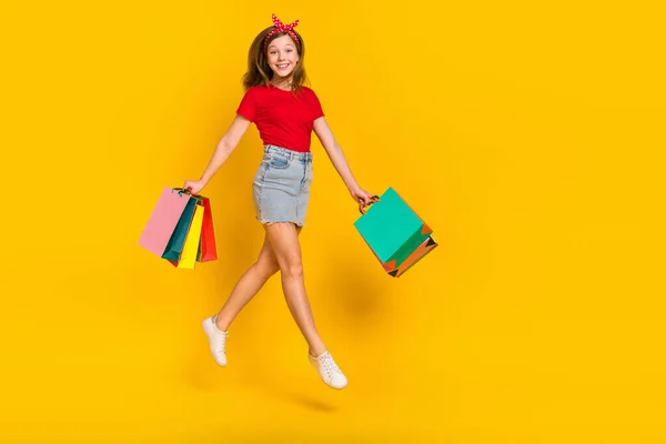 Ganzes Foto von netten Teenager Mädchen springen mit Taschen tragen T-Shirt Stirnband Rock Schuhe isoliert auf gelbem Hintergrund — Stockfoto