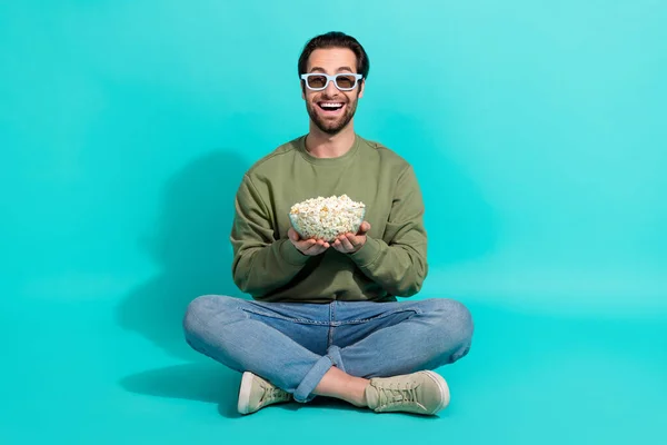 Full size photo of young cheerful man sit floor eat pop corn watch film isolated over turquoise color background — Stock Photo, Image