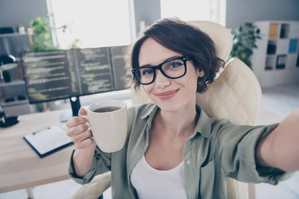 Foto de atraente senhora feliz sentado cadeira fazer selfie segurar xícara de café quente desfrutar de escritório local de trabalho dentro de casa — Fotografia de Stock