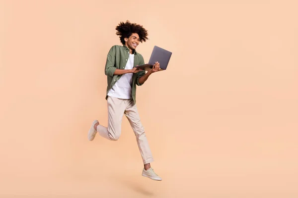 Volledige lichaamsomvang uitzicht van aantrekkelijke vrolijke trendy man springen met behulp van laptop werk geïsoleerd op beige pastel kleur achtergrond — Stockfoto