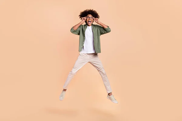 Vista completa del tamaño del cuerpo del atractivo chico alegre saltando tocando las especificaciones aisladas sobre fondo de color pastel beige —  Fotos de Stock